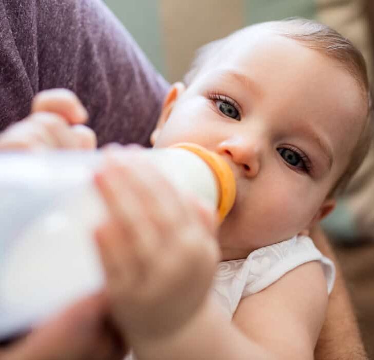 Mother lovingly holding her baby while feeding with a bottle in a warm, cozy home setting.